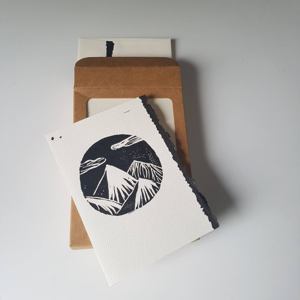 Homemade linocut mountain card placed on top of eco box