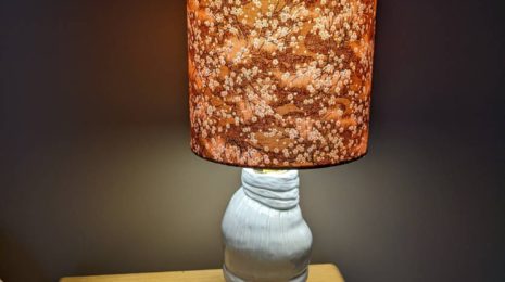 A photo of my homemade pottery lamp, lit up at night on a bedside table.