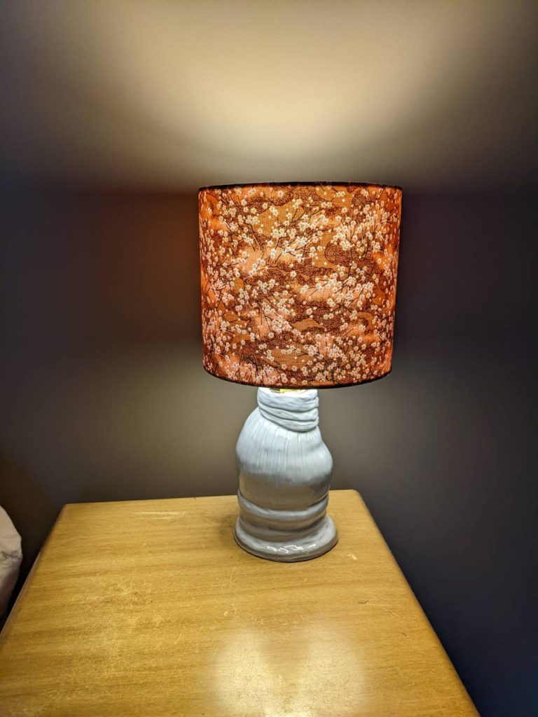 Pottery lamp with Japanese fabric shade lit up casting a warm glow.