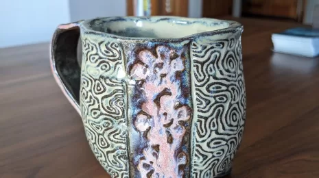 A three fotted potter mug in dark clay with texture of natural elements (flowers and topography)