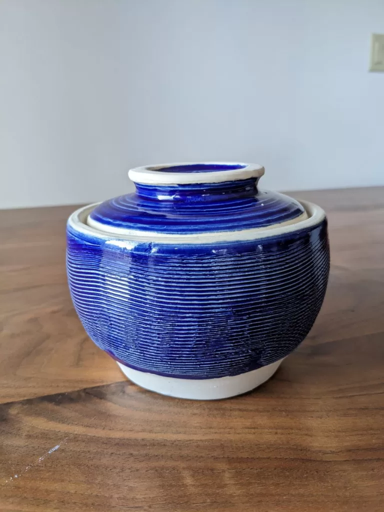 An eye-level view of a bright blue pottery cookie jar that has a practical twist - a lid that can be used as a plate.