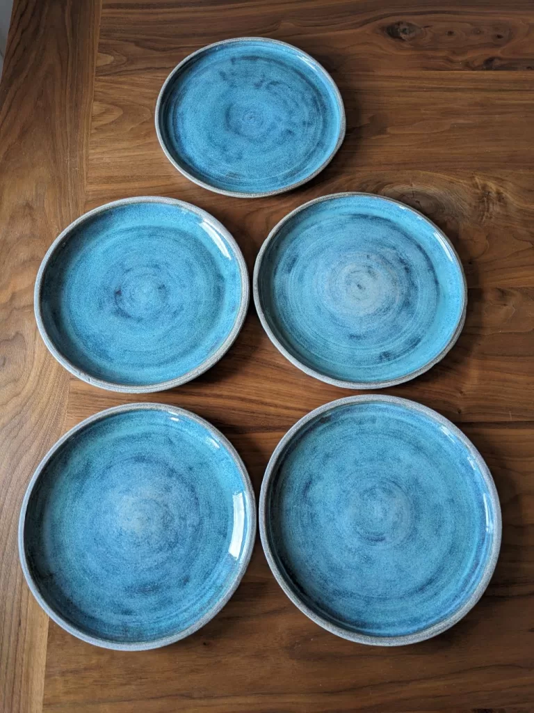 The final set of five pottery dinner plates displayed on a wooden table.
