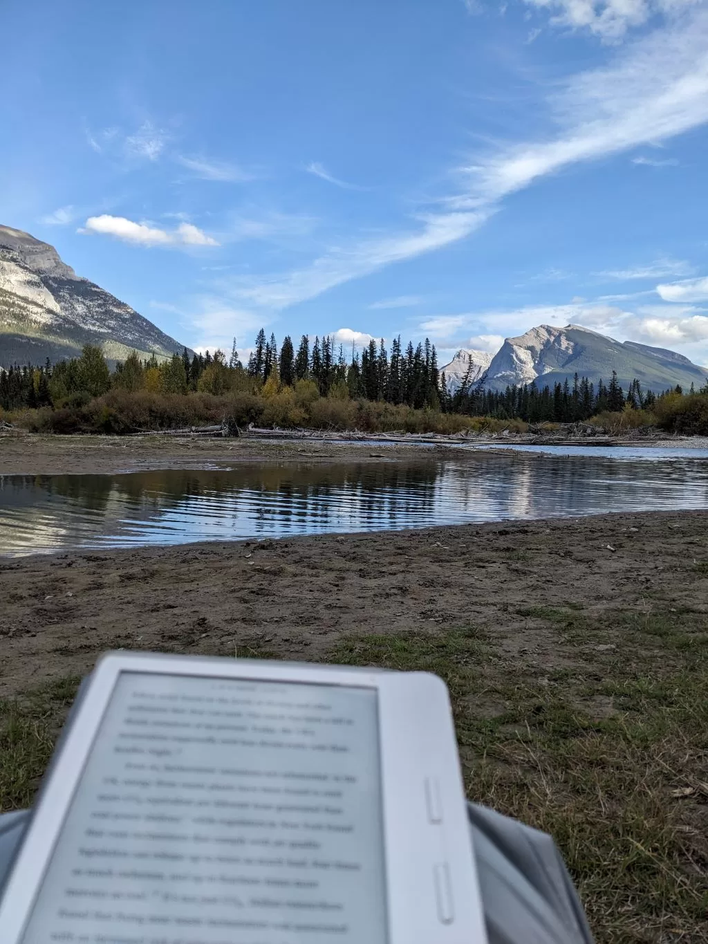 Someone reading an eReader beside a river in the rocky mountains. Featured in my post on my favourite books in 2023.